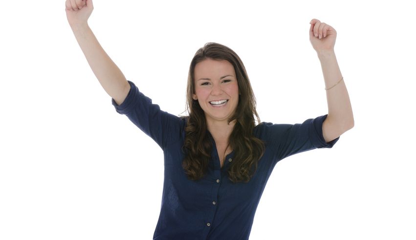 Junge dunkelhaarige Frau mit blauem Hemd reckt die Arme vor Freude nach oben und lacht