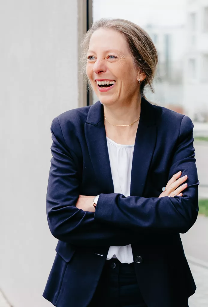 Beraterin Simone Gehr steht mit lachend und mit verschränkten Armen vor einem Bürogebäude