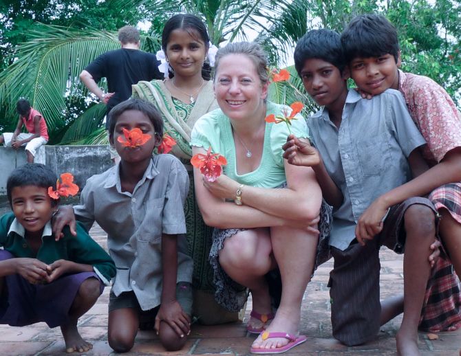 Simone Gehr kniet mit 4 indischen Kindern vor der Kamera. Alle halten eine rote Blume in der Hand.