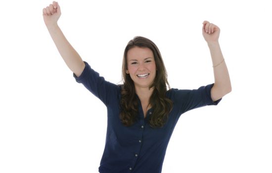 Junge dunkelhaarige Frau mit blauem Hemd reckt die Arme vor Freude nach oben und lacht