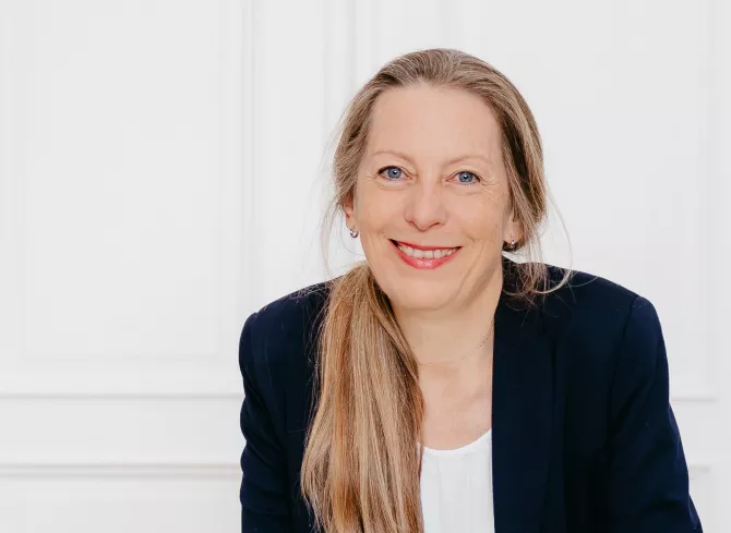 Simone Gehr in blauem Anzug und mit Pferdeschwanz beugt sich lächelnd nach vorne